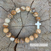 top view of the  Mens 'Thou Art With Me' Natural Stone Bead Cross Bracelets Picture Jasper against the cut surface of a log