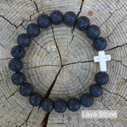 top view of the  Mens 'Thou Art With Me' Natural Stone Bead Cross Bracelets Lava Stone against the cut surface of a log