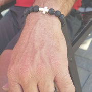 Close-up view of the  Mens 'Thou Art With Me' Natural Stone Bead Cross Bracelets Lava Stone on an arm